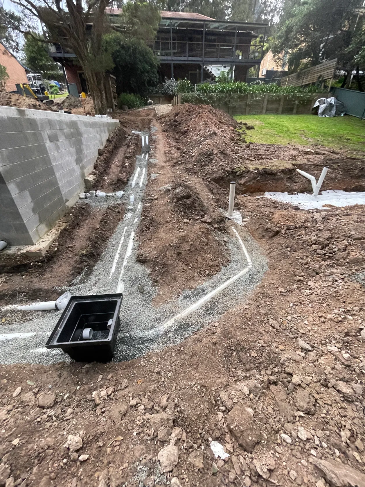 Black drainage pit and PVC pipe network in backyard excavation