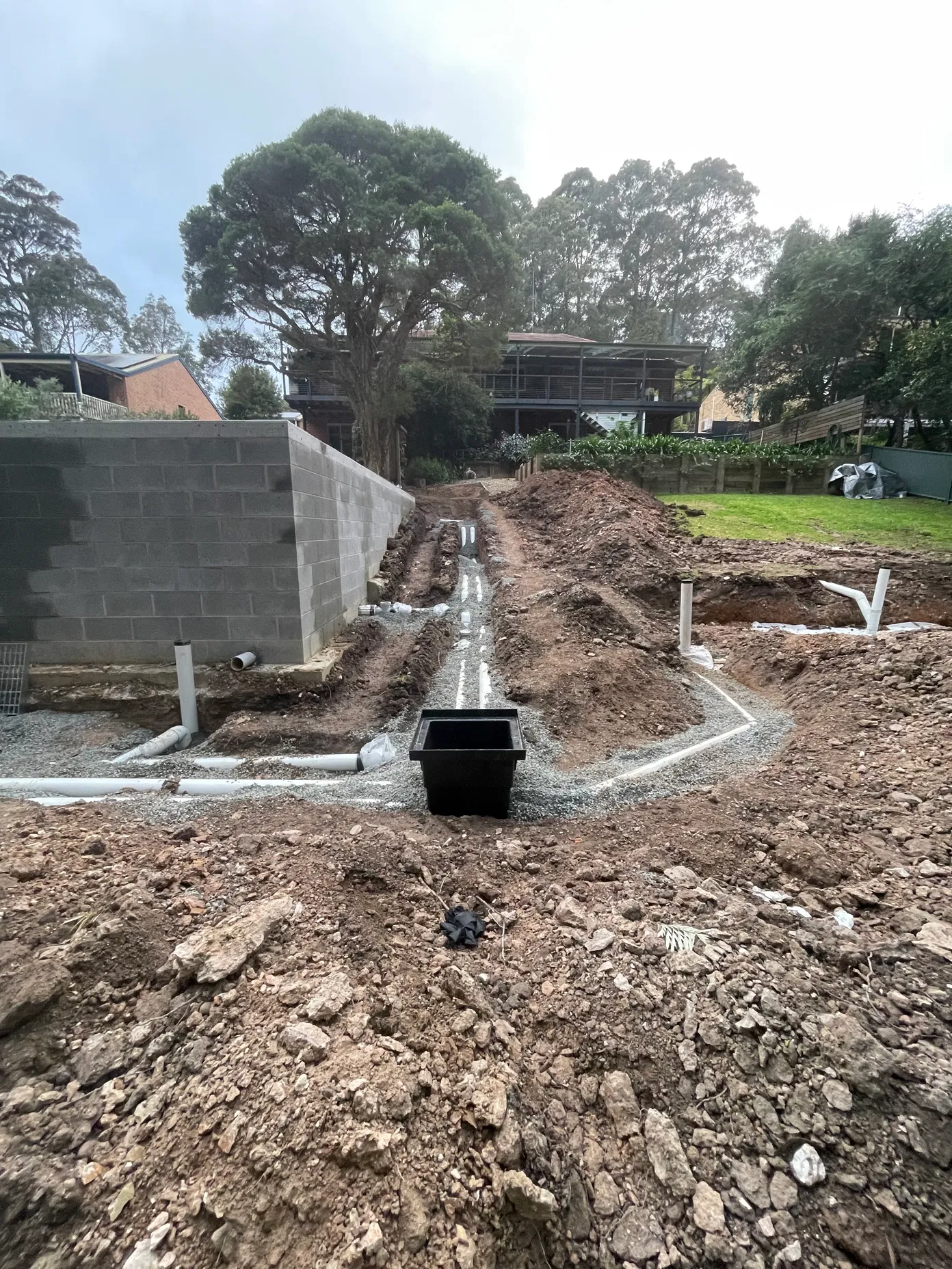 PVC drainage pipes in gravel trench beside concrete block retaining wall