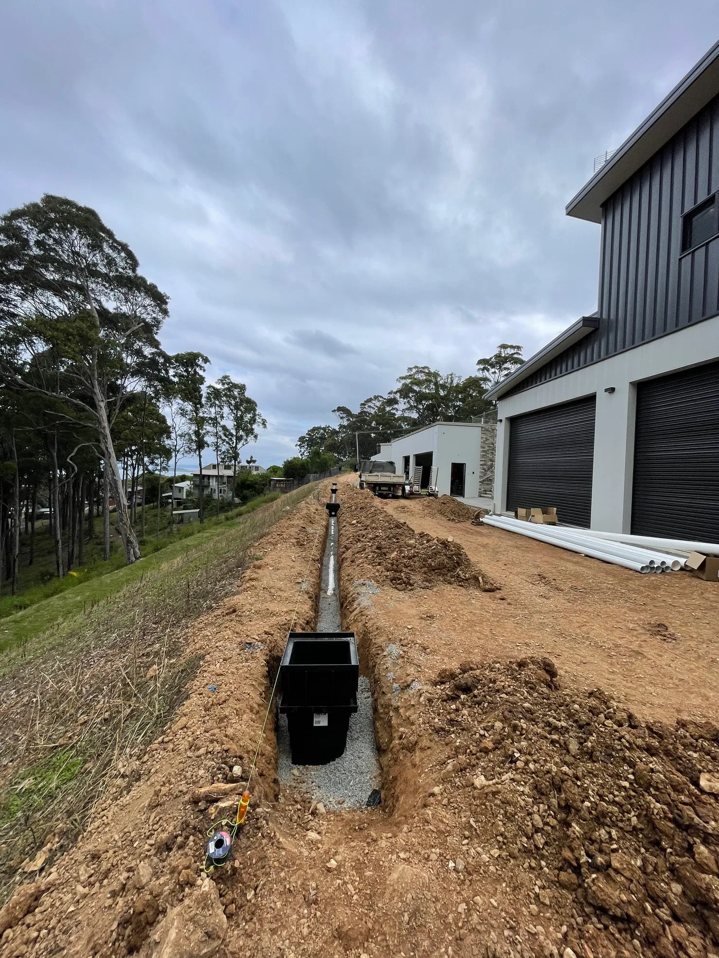 Drainage catch basins and channel installed in excavated trench beside building