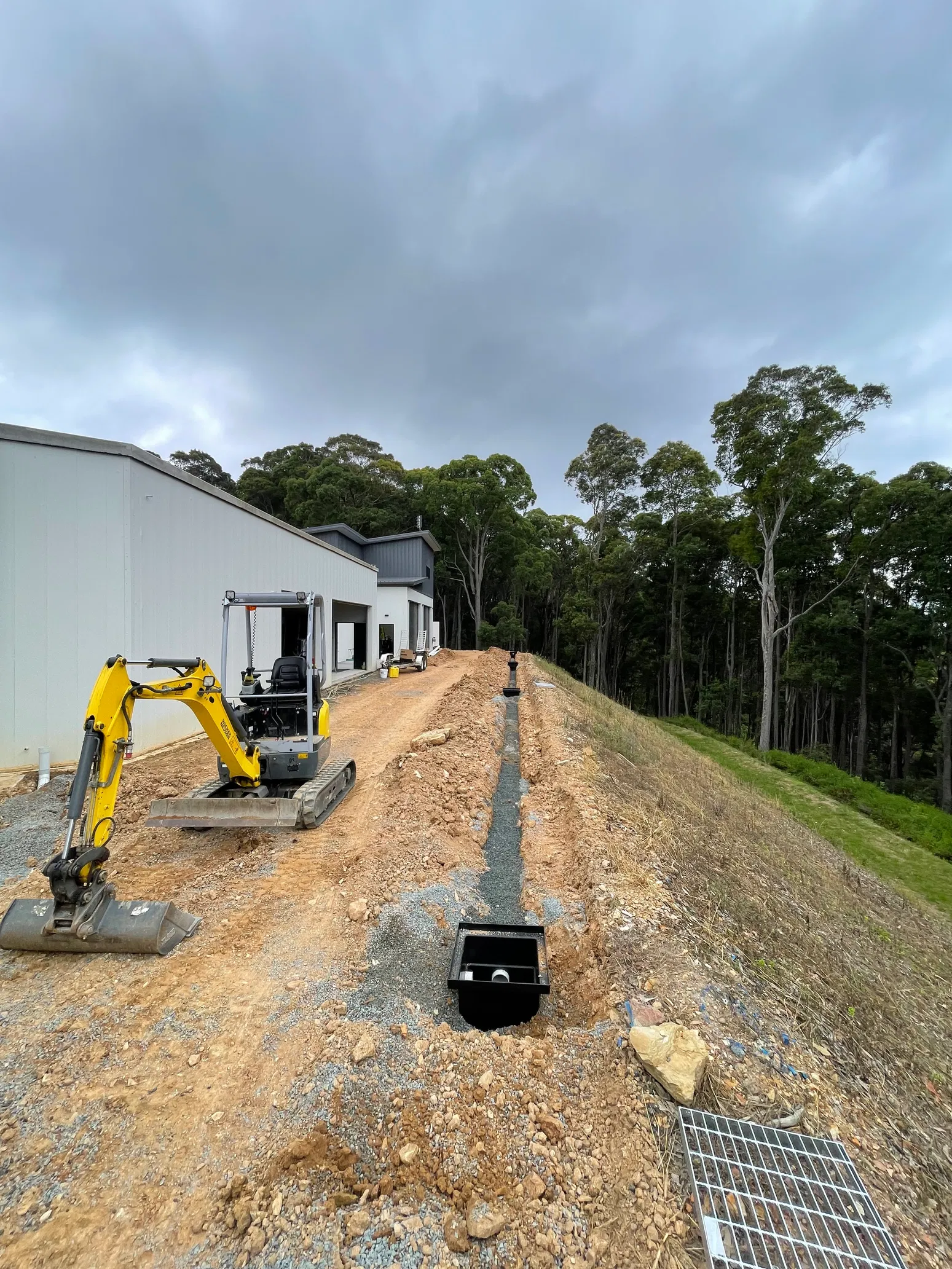 Mini excavator beside gravel drainage trench with catch basins