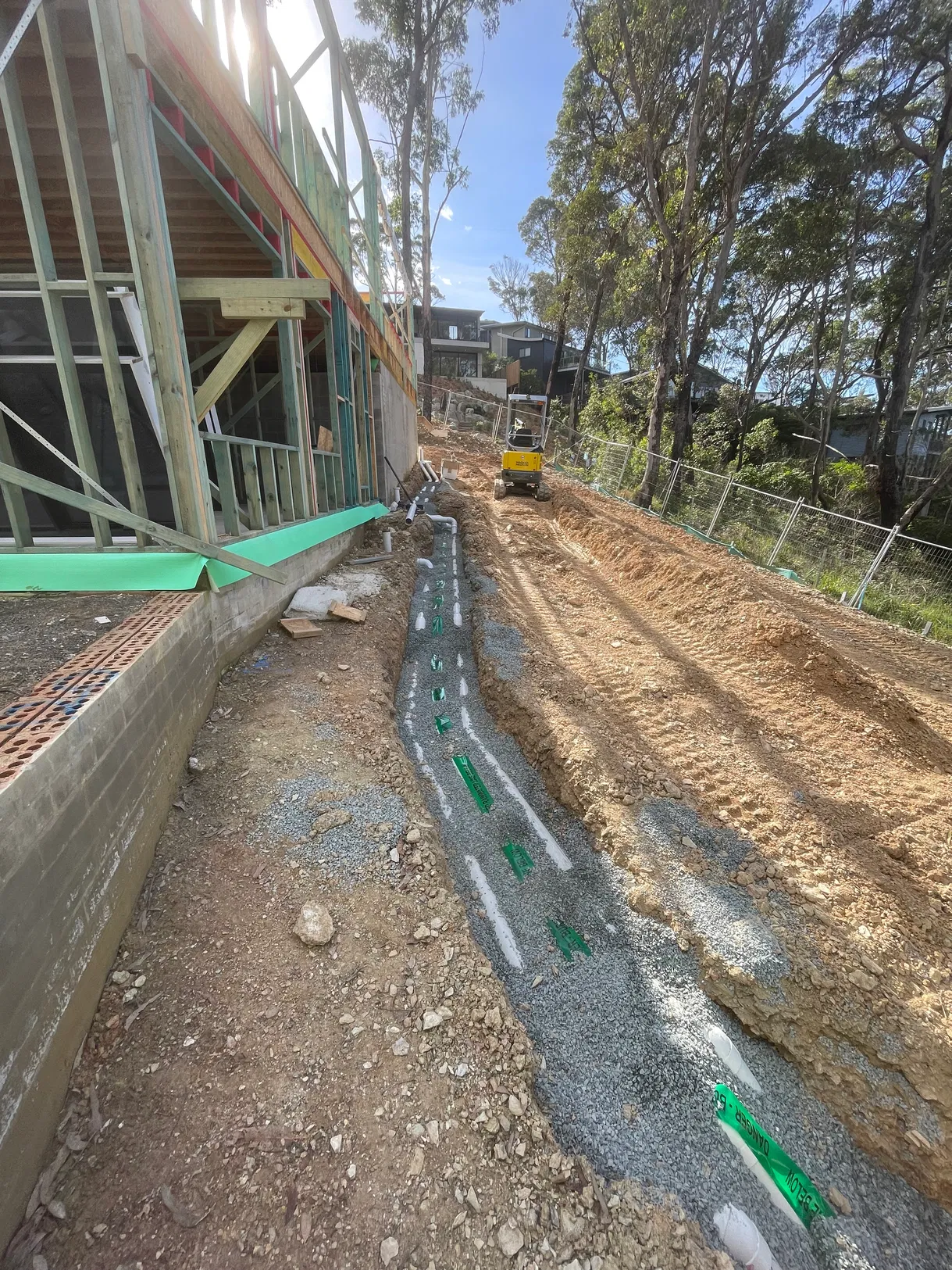 Sub-soil drainage pipes in gravel trench beside timber-framed house