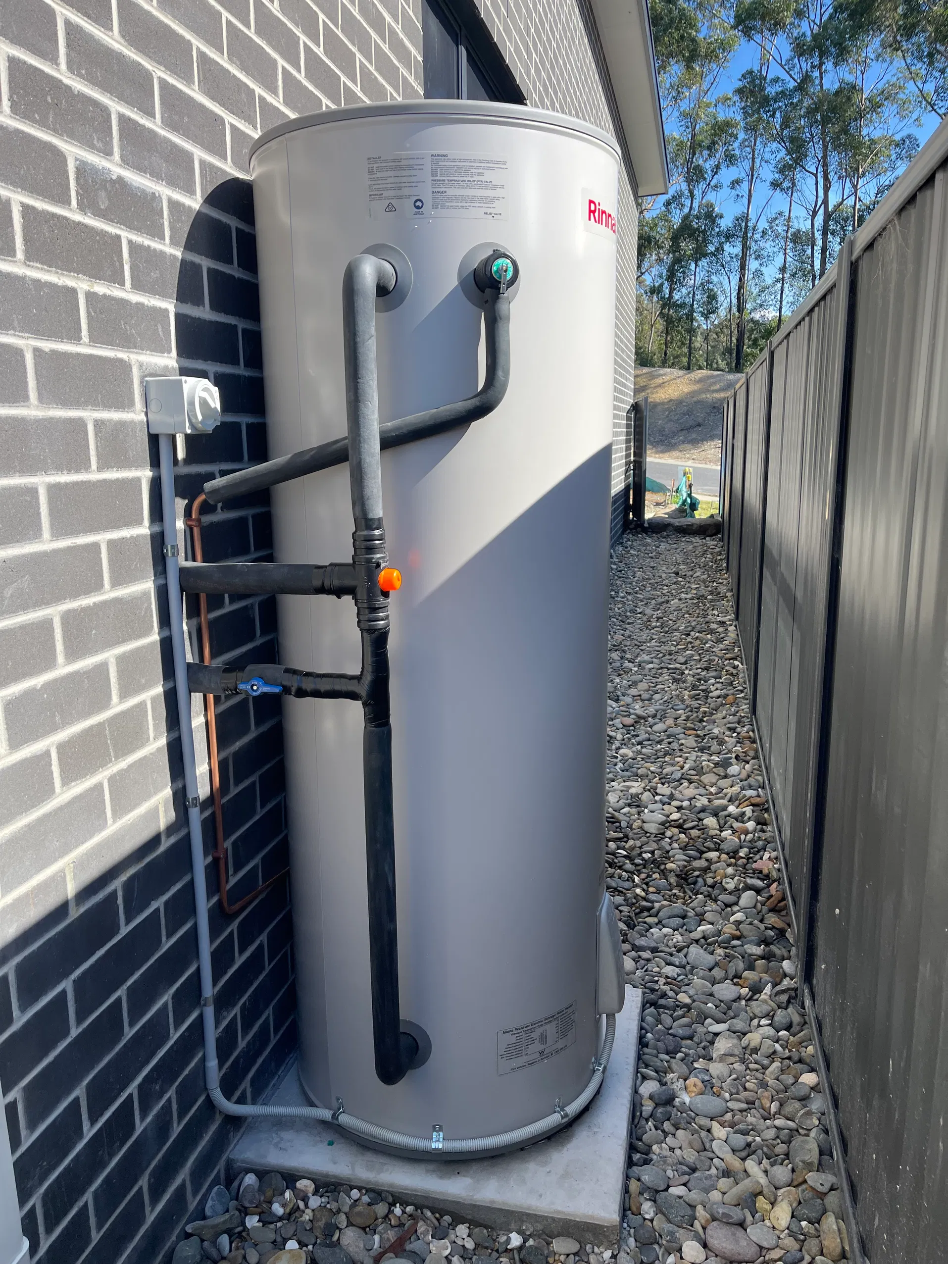 Outdoor Rinnai hot water storage tank installed against brick wall