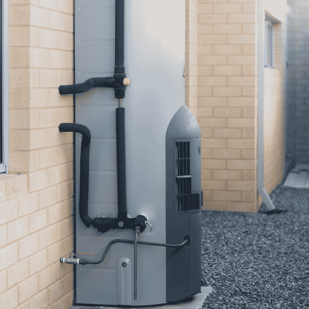 Outdoor heat pump hot water system installed against brick wall